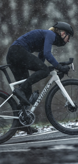 A cyclist wearing a helmet rides a white S-Works bike in snowy conditions.