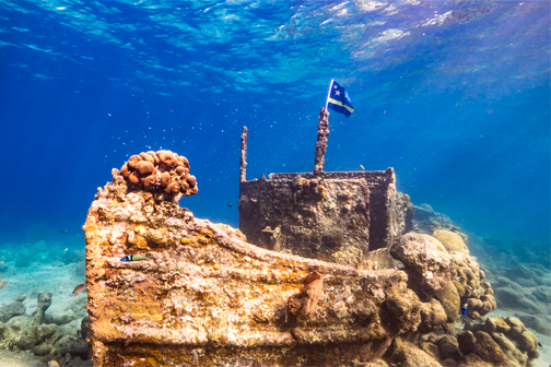 Tugboat bij Curaçao onder water, omringd door helderblauw zeewater, kleurrijk koraal en tropische vissen