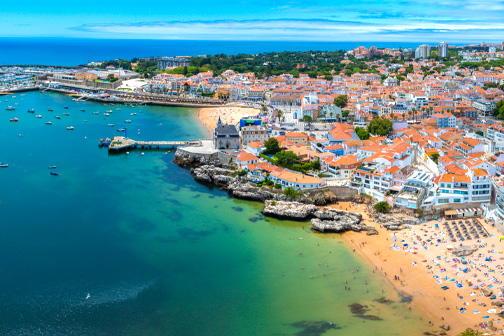 Cascais bij Lissabon met kleurrijke gebouwen langs de kust, een zandstrand en helderblauw water van de Atlantische Oceaan.