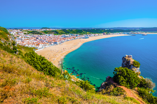 Uitzicht op Nazaré in Portugal met een breed zandstrand, witte huizen langs de kust en de Atlantische Oceaan op de achtergrond.