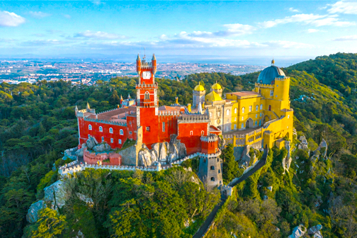 Paleis van Pena in Sintra met kleurrijke gele en rode torens, sierlijke architectuur en groene heuvels rondom het paleis.