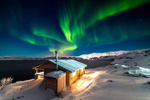 Houten huisje op een sneeuwvlakte naast een groot meer, met het noorderlicht in de lucht