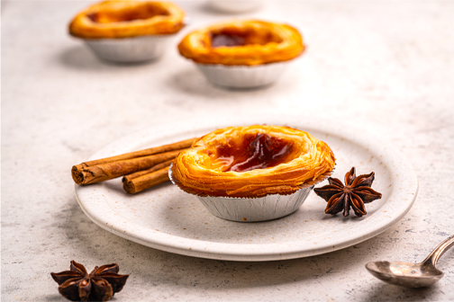 Portugese pastéis de nata met knapperig bladerdeeg en romige custardvulling, bestrooid met kaneel en poedersuiker.