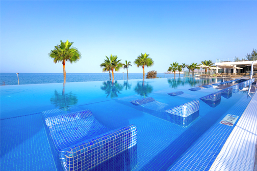 Infinity-zwembad met ligbedden in het water, palmbomen en panoramisch uitzicht over de zee bij RIU Gran Canaria.