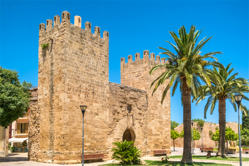 Porta del Moll in Alcúdia op Mallorca met historische stadspoort, oude stenen muren en een straat die door de poort naar de binnenstad loopt.