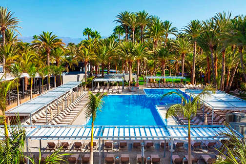Zwembad van RIU Palace Oasis, omringd door ligbedden en een weelderige palmentuin.