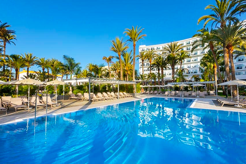 Ruim zwembad met ligbedden, palmbomen en het hotel van RIU Palace Palmeras op de achtergrond.