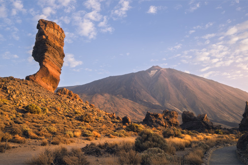 Vulkanisch landschap met de Teide op Tenerife, met rotsformatie op de voorgrond en zonlicht dat de berg en droge vegetatie warm kleurt.