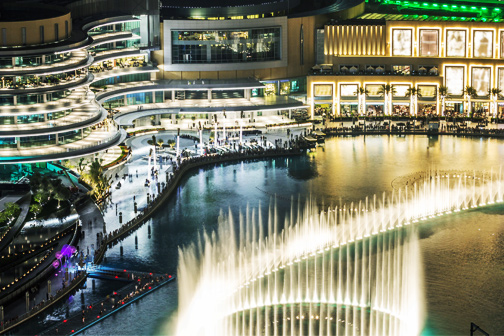 Een drukke boulevard bij fonteinen met dansend en lichtgevend water bij de Dubai Mall tijdens de nacht