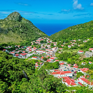 Bergdorp op Saba met rode daken tussen groene heuvels, met uitzicht op de helderblauwe Caribische Zee.