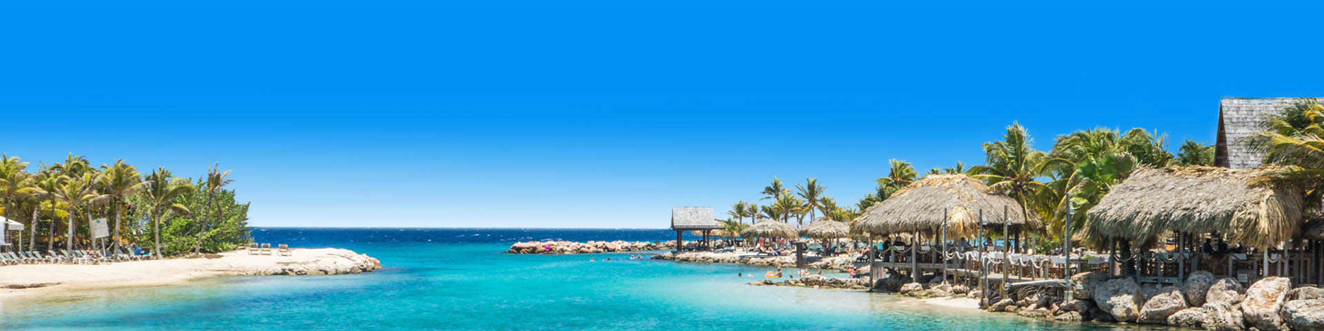 Rotsachtig stran aan turquoise zee in Curaçao met cabana's