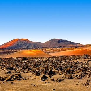 Strand op Lanzarote met donkere lavarotsen, helderblauw water en een ruige kustlijn onder een zonnige lucht.