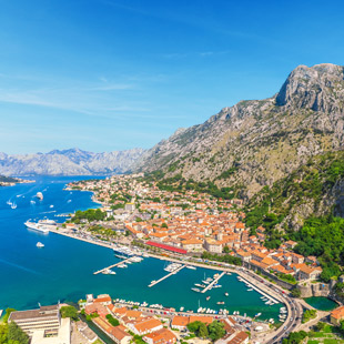 Baai van Kotor met blauwe zee, oranje daken, haven en hoge bergen op de achtergrond.