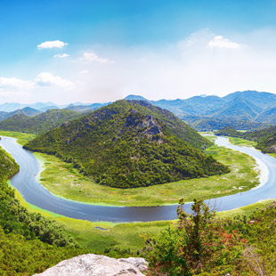 Skadar meer met een bochtige rivier rond een groene heuvel en bergen in de verte.