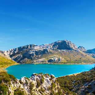 Mirador de l’Embassament op Mallorca met uitzicht over een blauw stuwmeer, omringd door groene bergen en rotsachtige hellingen.